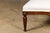 A French wooden ottoman from circa 1900 with tapering cylindrical legs, carved giltwood rosettes and muslin double welt...