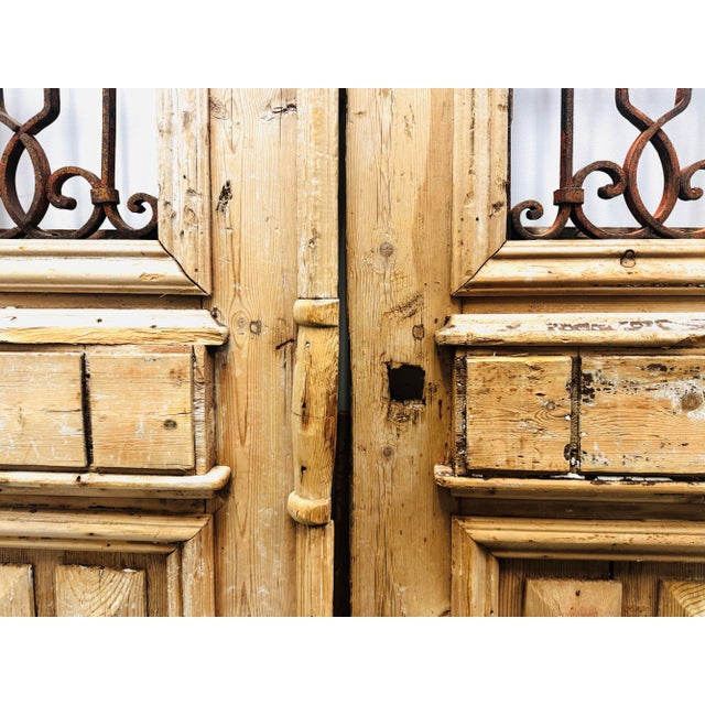 Tall antique French double doors featuring original wood panels and decorative wrought iron grilles. Weathered patina and...