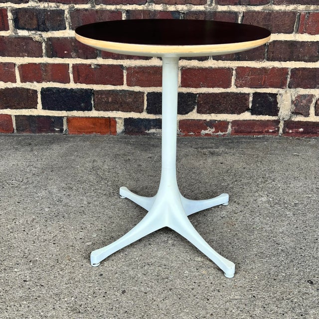 This is a mid century George Nelson for Herman Miller tulip side table. It has an off-white metal pedestal base with a...