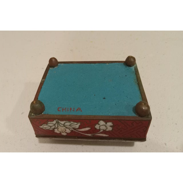 Early 20th century lidded cloisonné box. Brass construction with hinged lid. Ruby red decorated with colorful flora....