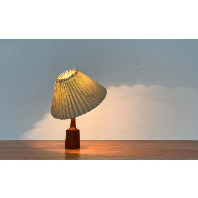 Danish table lamp with a teak base from the 1960s. The conical pleated shade sits directly on the bulb with a clamp. This...