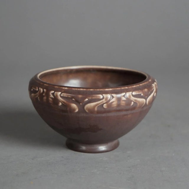 An antique Arts and Crafts bowl by Rookwood offers tapered form with stylized foliate band and maker mark on base as...