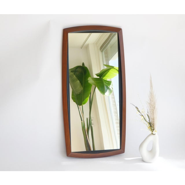 A vintage Danish wooden wall mirror made out of teak with a beautiful frame with a black detail inside. The mirror is...