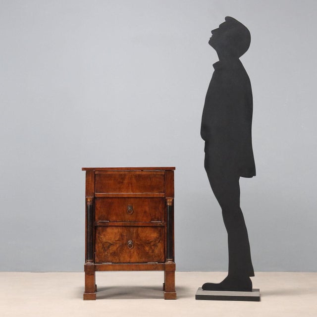 Empire walnut bedside table. Top and drop-front doors, turned and ebonized half columns with gilded capitals and bases....