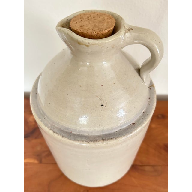 Antique late 1800s American stoneware jug. It is a light sand or beige color with brown accenting. There is an impressed...