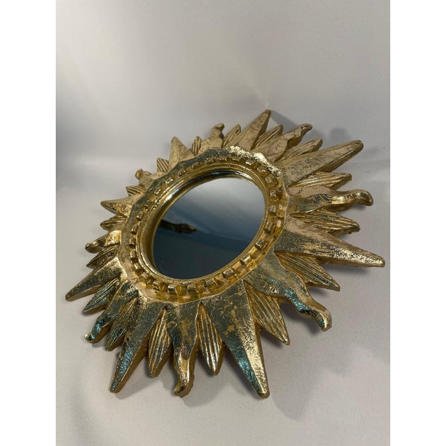 A very bright and shiny gold gilded 12.5" Sunburst Wall Mirror from circa the Mid 20th Century. This fabulous mirror...