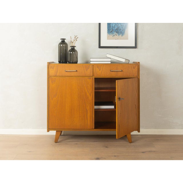 Classic chest of drawers from the 1950s. Ash veneer body with two drawers, two doors, two shelves, and angled legs. The...