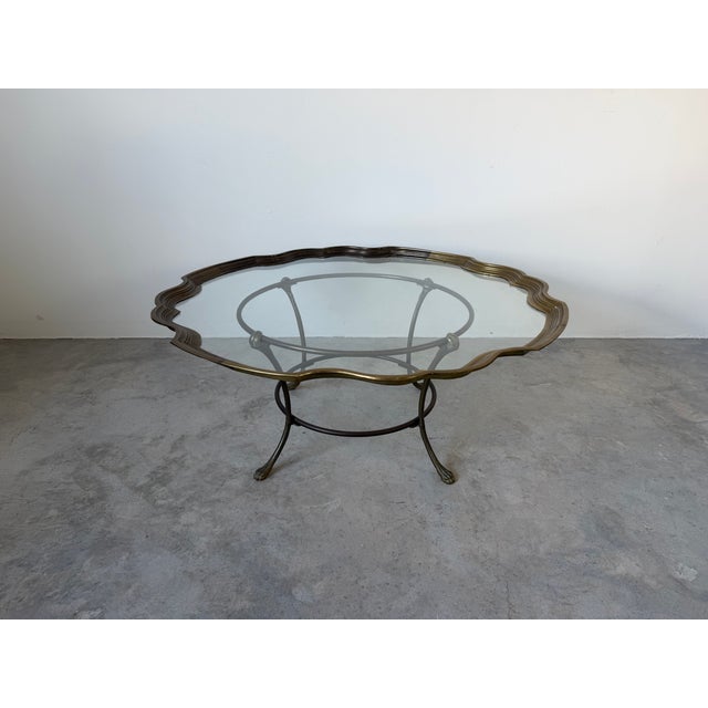 Elegant vintage coffee table featuring a sculptural brass base with stylized claw feet and a beautifully shaped scalloped...