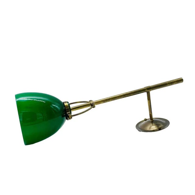 Wall lamp with green glass diffuser and opaline interior, it has a brass stem and a circular base. The lamp is made in...
