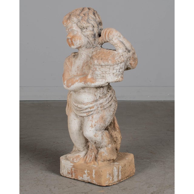 A French terracotta garden statue of a cherubic child holding a flower basket. Good condition with fading white paint and...