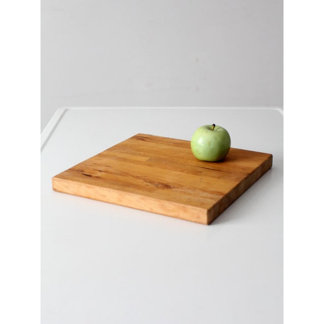 Vintage handmade wood cutting board featuring a thick, square form and warm honey-toned grain. The surface displays...