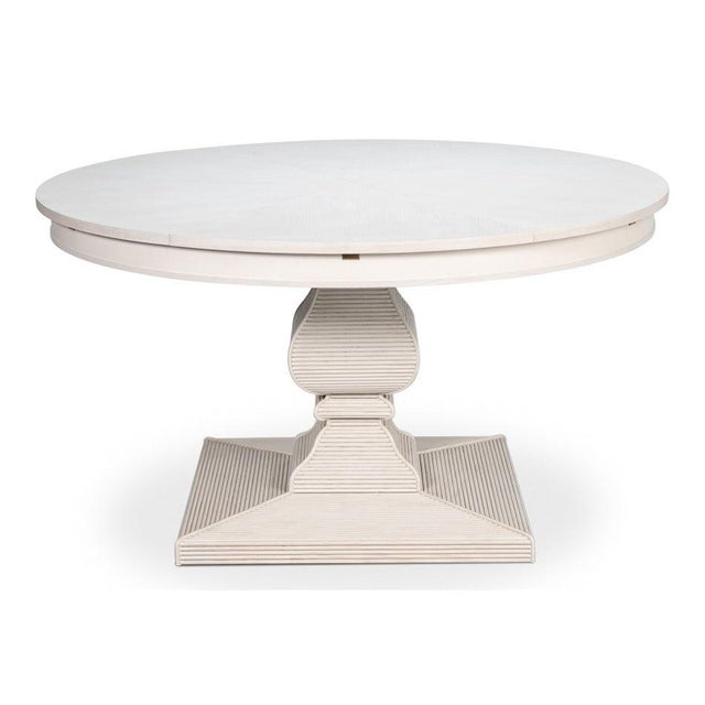 A densely carved pedestal gives the pale circular top a substantial architectural foundation. The round top reads as one...
