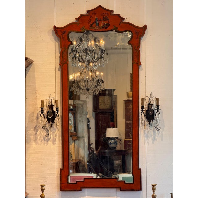 A red chinoiserie mirror, the shaped pagoda crest painted with two figures beside a fence before a pagoda and willow,...