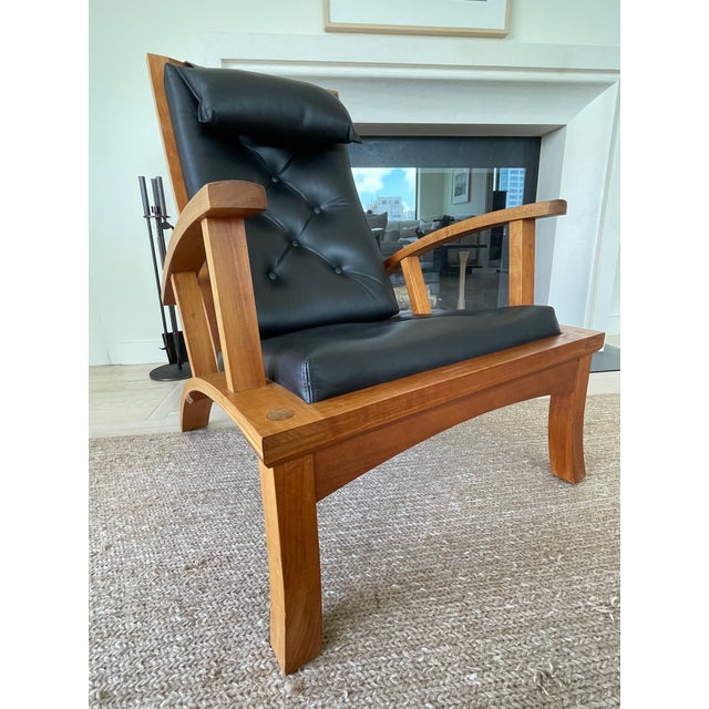 Handcrafted Thomas Moser Lolling Chair with matching ottoman in solid cherry and tufted black leather. One of the most...