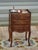 Elegant bedside table with three drawers and raised edges on three sides of the top. The tall, slender base features four...