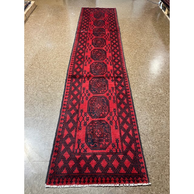 Hand-knotted Afghan Khal Mohammadi runner featuring a row of geometric guls on a deep red field with dark navy accents and...