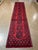 Hand-knotted Afghan Khal Mohammadi runner featuring a row of geometric guls on a deep red field with dark navy accents and...