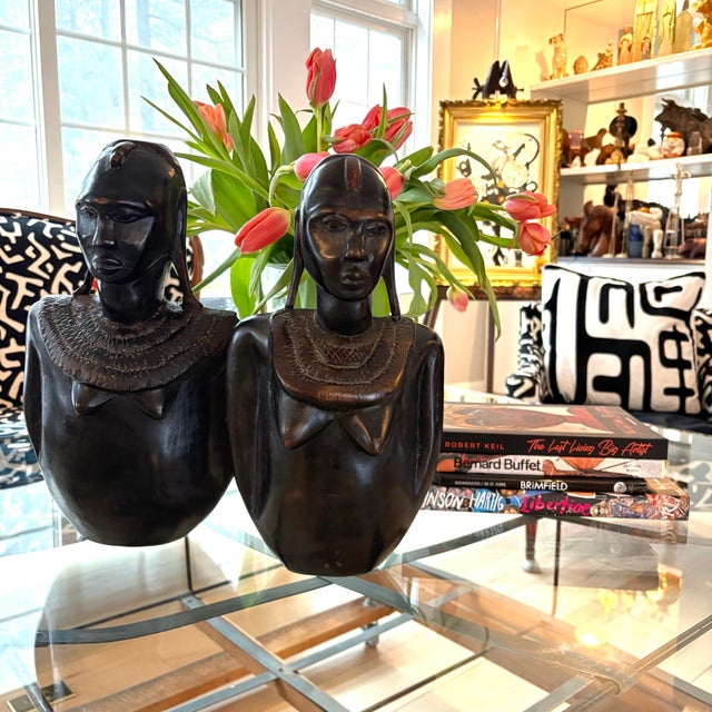 A striking pair of vintage hand-carved wooden bust sculptures featuring elongated forms, serene expressions, and...
