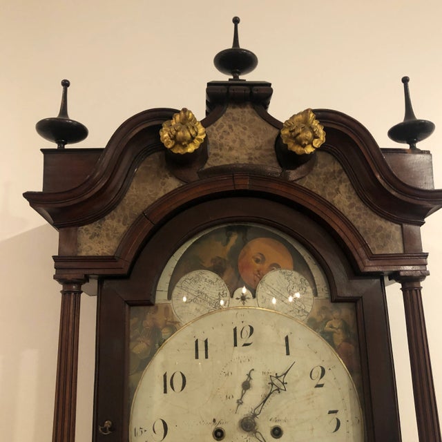 Antique English Mahogany tall clock featuring draped mahogany on front panels and a shaped hood with three finials on top....