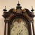 Antique English Mahogany tall clock featuring draped mahogany on front panels and a shaped hood with three finials on top....