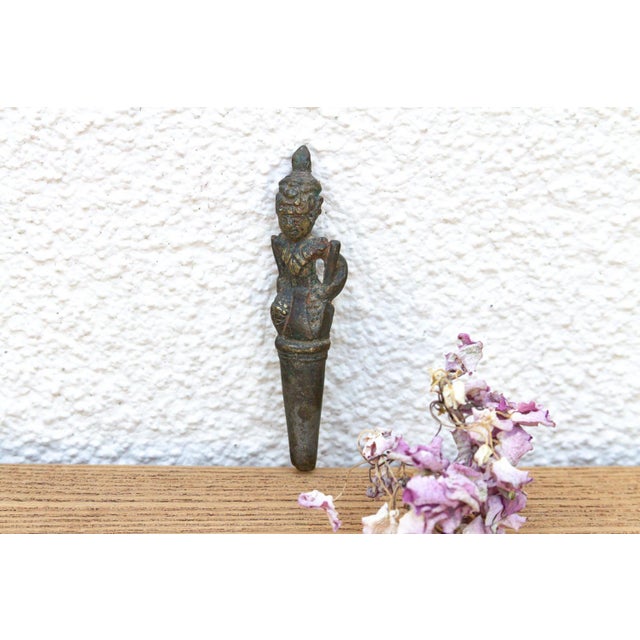 A fascinating, heavily crusted micro-artifact featuring a stylized kneeling guardian figure atop a tapered structural peg,...