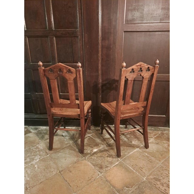 A charming pair of late 19th-century English pitch pine hall chairs, each with a beautifully shaped dished seat displaying...