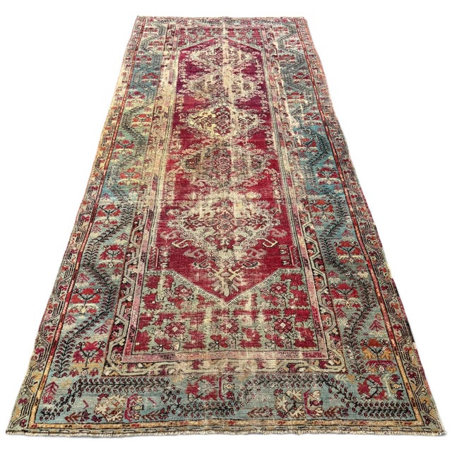 A richly patterned antique Turkish runner with the faded beauty and intricate detail of a well-loved textile. The deep red...