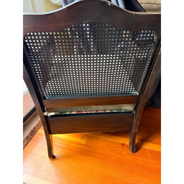 A commanding late 19th century cane armchair with an ebonized hardwood frame, caned back and side panels, scrolled open...
