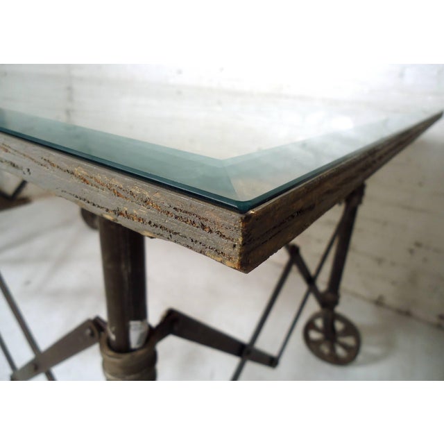 Custom built industrial accordion table features glass on top of a wood table top, accordion base that easily closes, on a...