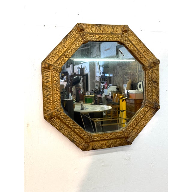 This octagonal mirror is framed in sculpted gilt iron, featuring a deeply textured surface that alternates between linear...