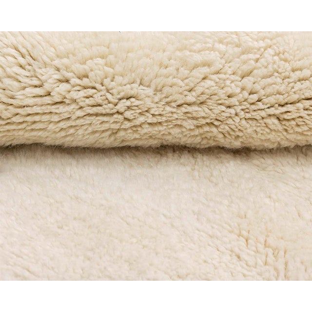 Serene hand-knotted wool rug in a soft Ivory color, featuring a subtle asymmetric cross pattern that adds a touch of...