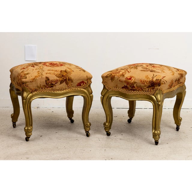 Pair antique footstools or benches on casters with floral upholstery. Good condition overall with slight finish loss due...