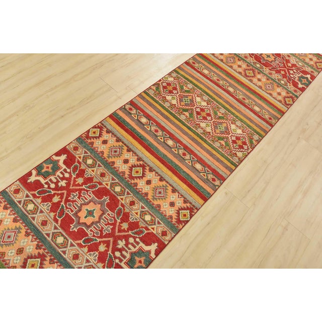A tribal Khorjin runner hand-knotted with fine wool on a cotton foundation. This rug features multicolored stripes adorned...