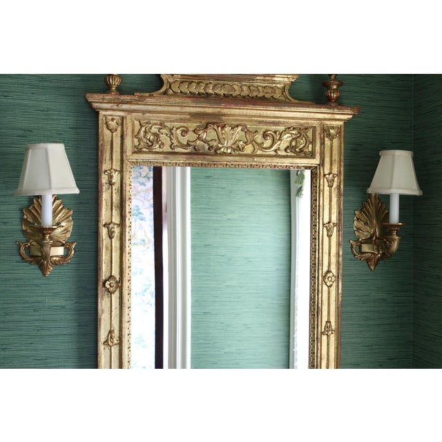 A grand gilt Neoclassical style wall mirror with a stylized crest with two kissing birds, tied husks, rocaille and foliate...