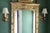 A grand gilt Neoclassical style wall mirror with a stylized crest with two kissing birds, tied husks, rocaille and foliate...