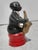A ceramic figurine in the form of a black male musician playing the trumpet while sitting on a red ottoman. The musician...