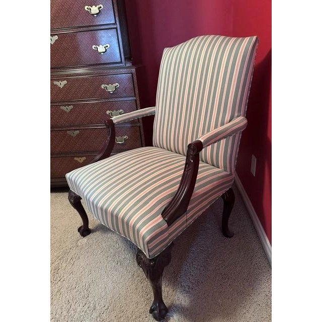 The vintage armchair features classic Queen Anne styling characterized by its elegant scroll armrests and dark wooden...
