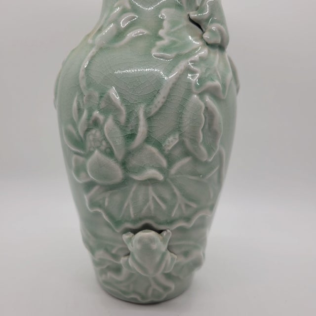 Celadon green glazed porcelain vase features an intricate relief design of lotus flowers, large leaves, and a small frog....