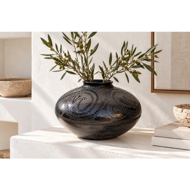 A squat, rounded black pottery vessel signed on the base Yolanda Quezada, with a short collar neck and a softly flared...
