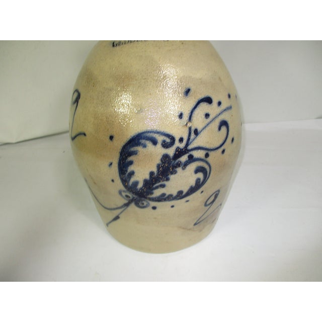 . Antique Beige handmade stoneware jug inscribed Geddes, NY. It is hand decorated with a cobalt blue floral design. This...