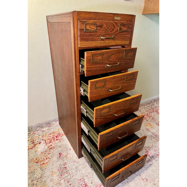 Seven deep drawers in richly figured oak have their original brass label holders and bail pulls. Each drawer runs on metal...