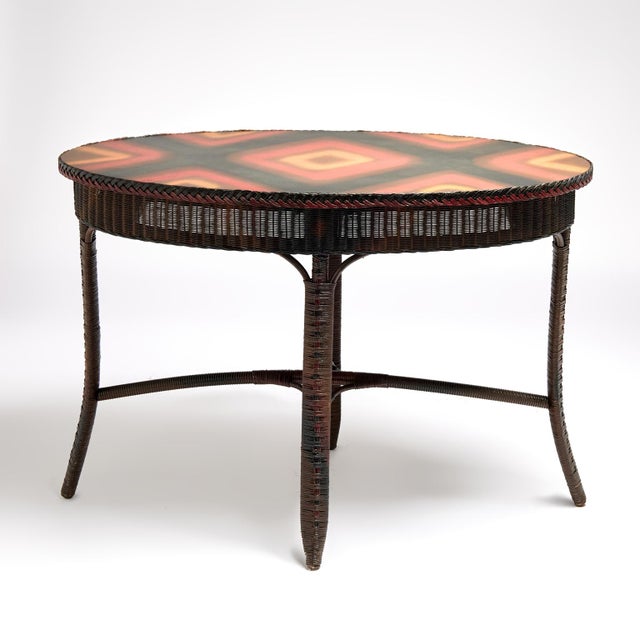 Spirited antique oval table handcrafted in stick wicker and woven reed featuring the original painted top decorated with...
