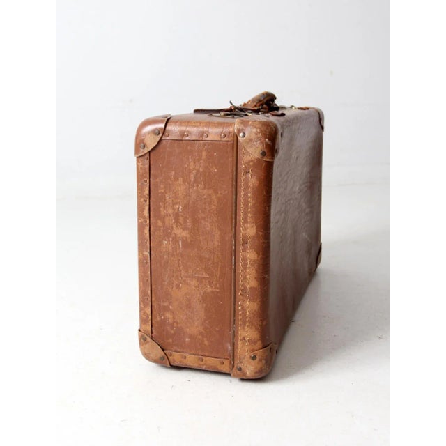 This vintage leather suitcase from the 1930s–1940s features reinforced leather corners, a matching leather handle, and...