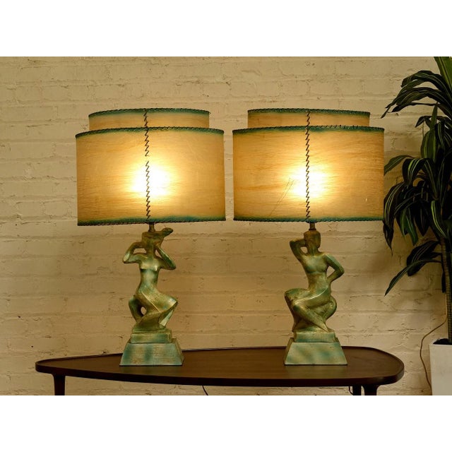 A striking pair of vintage table lamps featuring sculptural figural bases paired with distinctive double-panel shades....