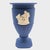 In the quiet dignity of dark blue, this porcelain urn whispers of antiquity. Pale figures in bas-relief drift across its...