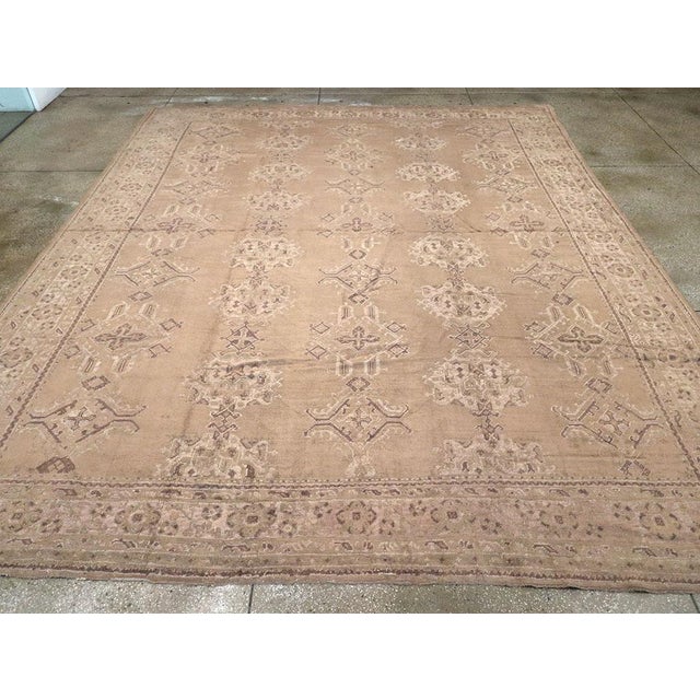 A soft brown tone uncluttered ground supports five columns of iconic Oushak-style Harshang palmettes and elaborate lozenge...