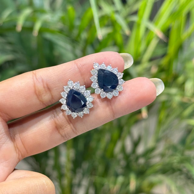 These halo stud earrings feature 8.01 carats of pear-cut blue sapphires, set in 14k white gold. Each center stone measures...