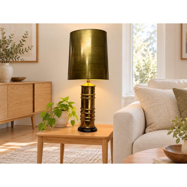 A striking Mid-Century Modern table lamp featuring a brutalist-style gold-tone cylindrical body with tiered, ridged...