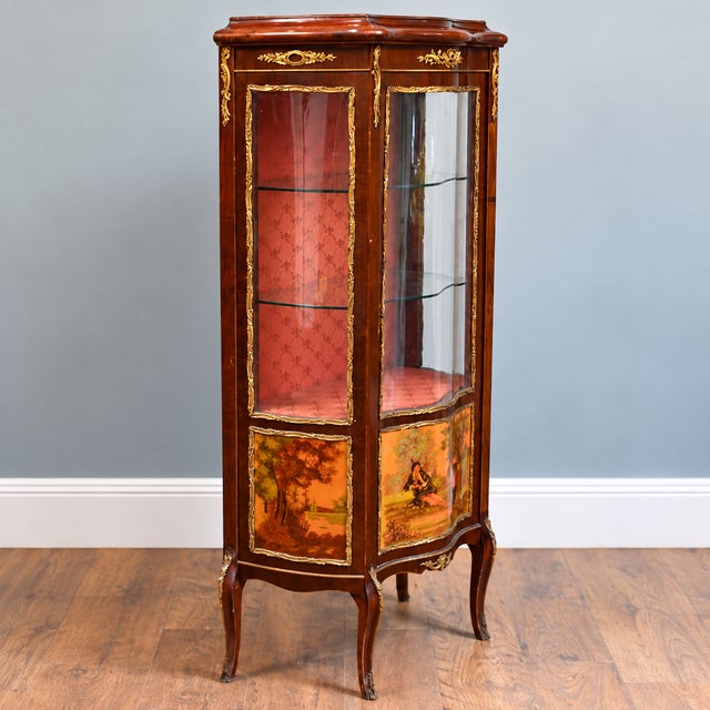 An elegant Louis XV style display cabinet with a glazed door and curved glazed sides. The cabinet has two glass shelves...