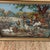 This is a framed needlepoint (or petit point–style) textile artwork depicting a rustic farmyard scene. The scene shows...
